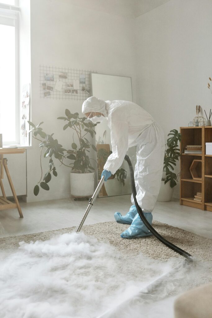 A Woman in PPE Disinfecting a Carpet